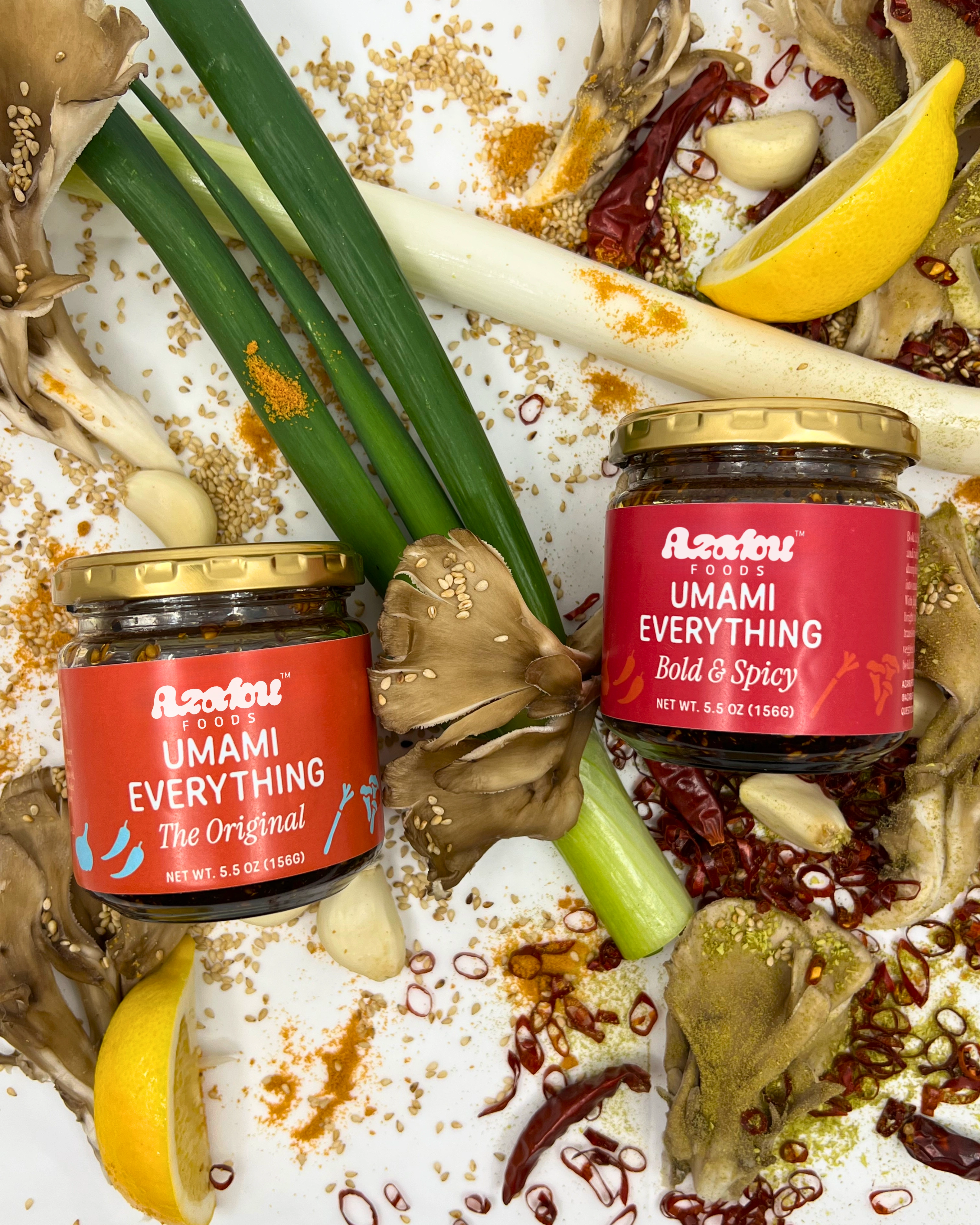 Jars of Azabu Foods’ Umami Everything – The Original and Bold & Spicy – surrounded by fresh ingredients including maitake mushrooms, green onions, dried chili peppers, sesame seeds, and yuzu, highlighting the bold Japanese flavors of the condiments.